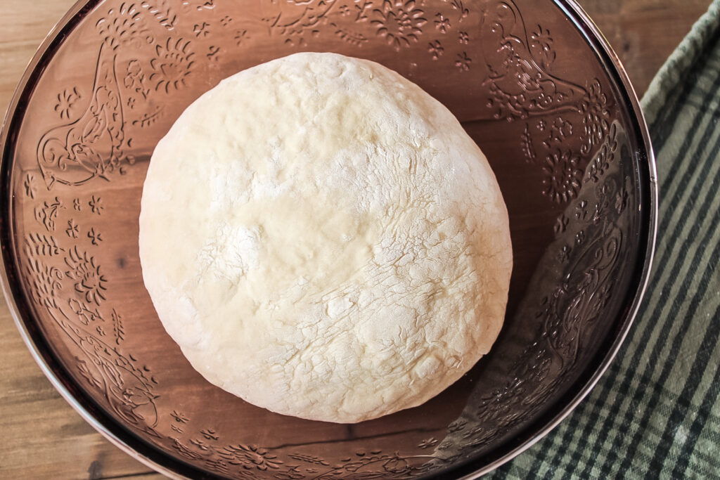 Ball of Dough in Mixing Bowl on Wood Surface with Towel